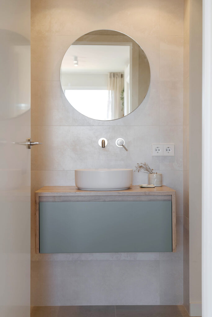 Baño con espejo redondo, lavabo sobre encimera y mueble suspendido