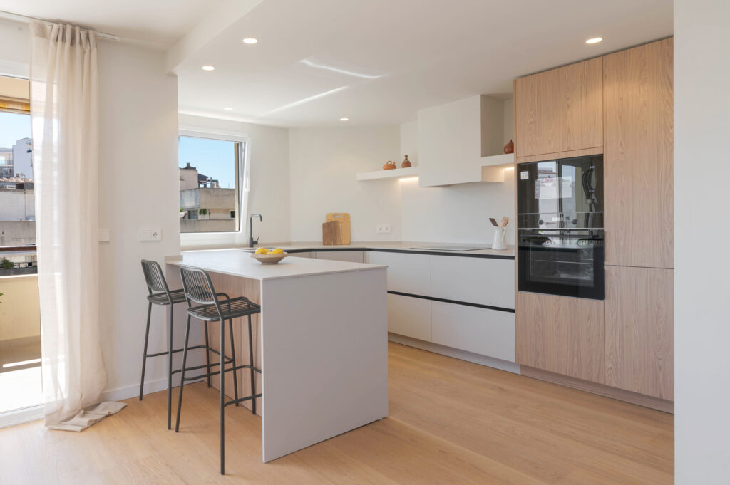 Cocina blanca y de acabado madera con barra, taburetes y luz natural