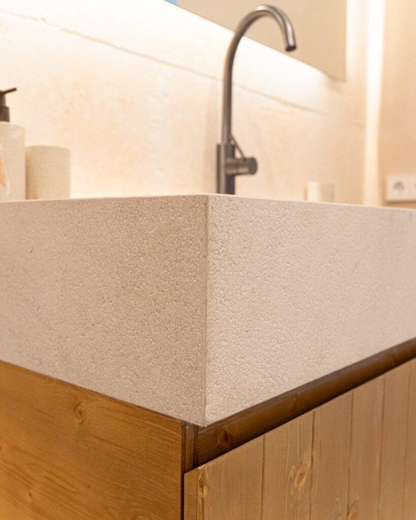 Detalle de lavabo rectangular de acabado pétreo sobre mueble de madera y grifería negra