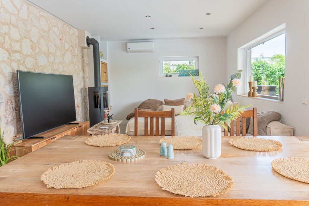 Salón-comedor con pared de piedra, estufa y mesa de madera junto al ventanal
