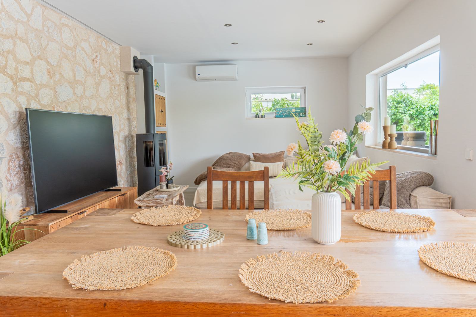 Salón-comedor con pared de piedra, estufa y mesa de madera junto al ventanal