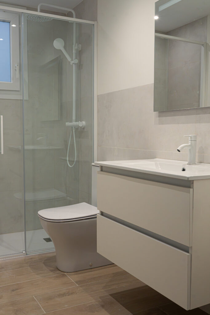 Baño reformado con ducha acristalada, mueble de lavabo suspendido e inodoro