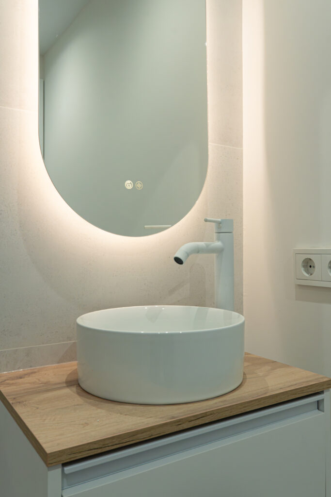 Lavabo sobre encimera con grifería blanca y espejo ovalado retroiluminado