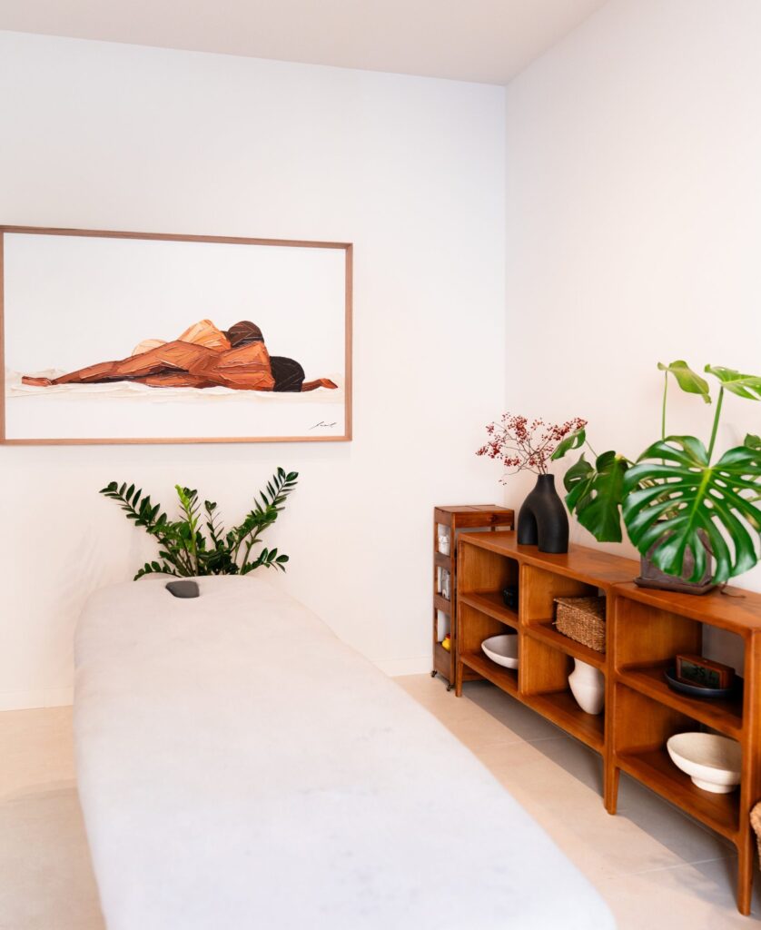Sala de masaje con camilla, mueble de madera y monstera