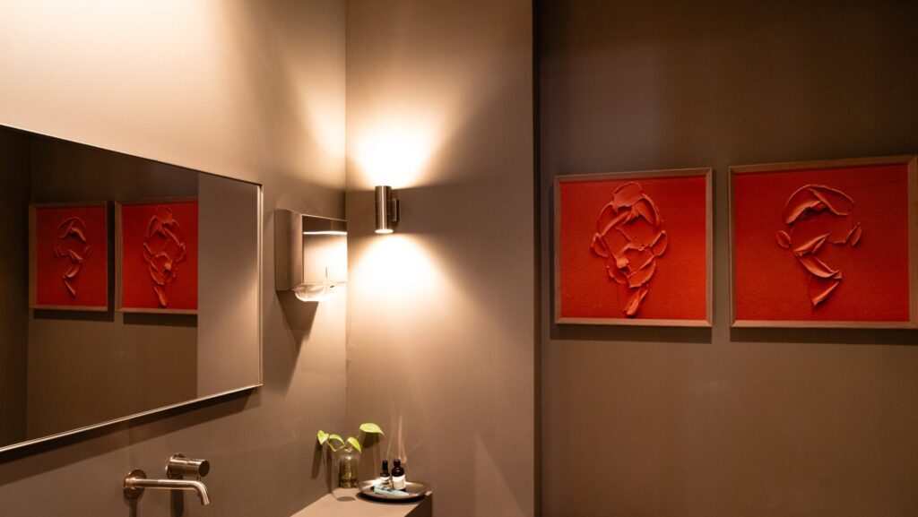 Baño en tonos oscuros con aplique de luz y cuadros rojos